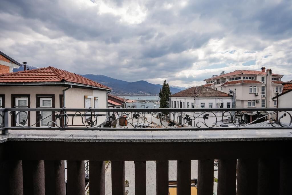 A balcony with a railing, buildings in the background, and a cloudy sky.