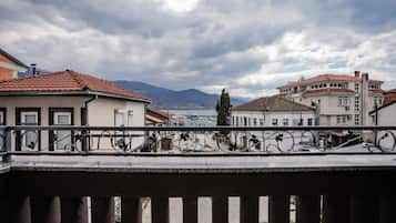 A balcony with a railing, buildings in the background, and a cloudy sky.