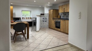 A modern kitchen with wooden cabinets, a built-in oven, and a dining area with a table and chairs.