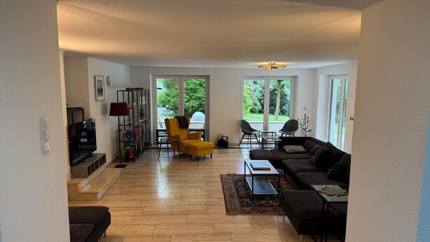 A spacious living area with a sofa, chairs, a TV, and a bookshelf.