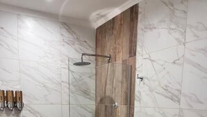 A bathroom with a shower, toilet, bidet, and marble tiles.
