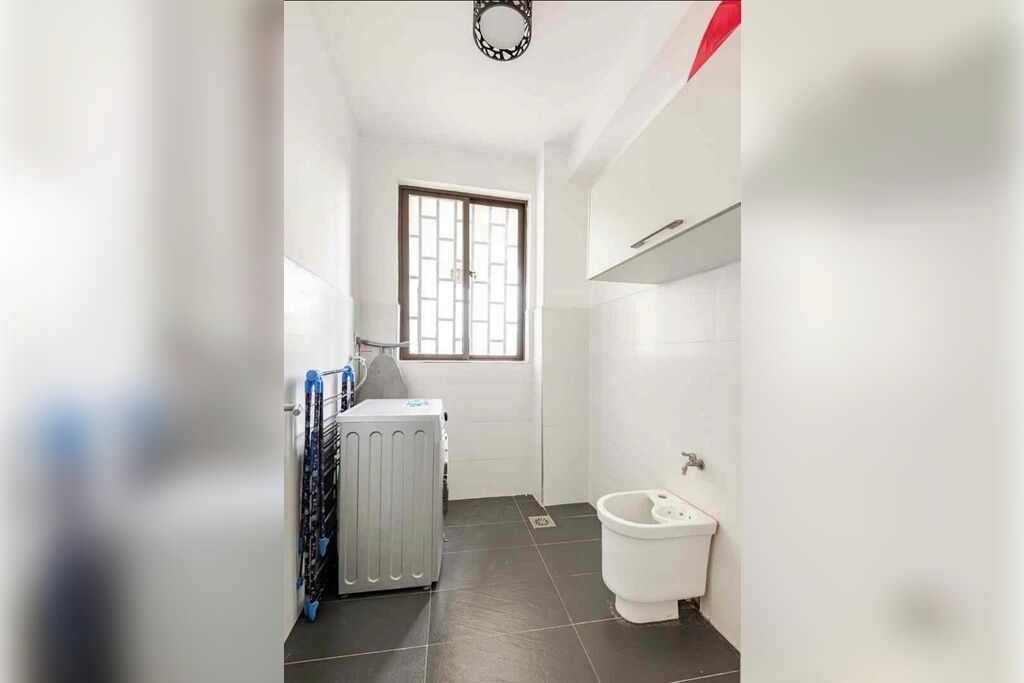 Ein kleines, schmales Badezimmer mit Heizkörper, Toilette und Fenster mit dekorativem Gitter.