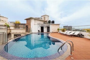 Ein Pool auf dem Dach mit freiem Blick auf die Stadtlandschaft, ein überdachter Bereich mit Liegestühlen und ein Hauseingang.
