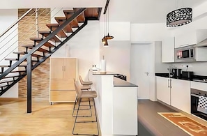 Eine moderne Küche mit einer zentralen Kochinsel, Barhocker, einer Treppe und einer hängenden Pendelleuchte.