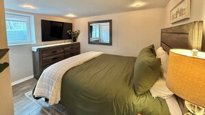 A bedroom with a bed, dresser, TV, and a window.