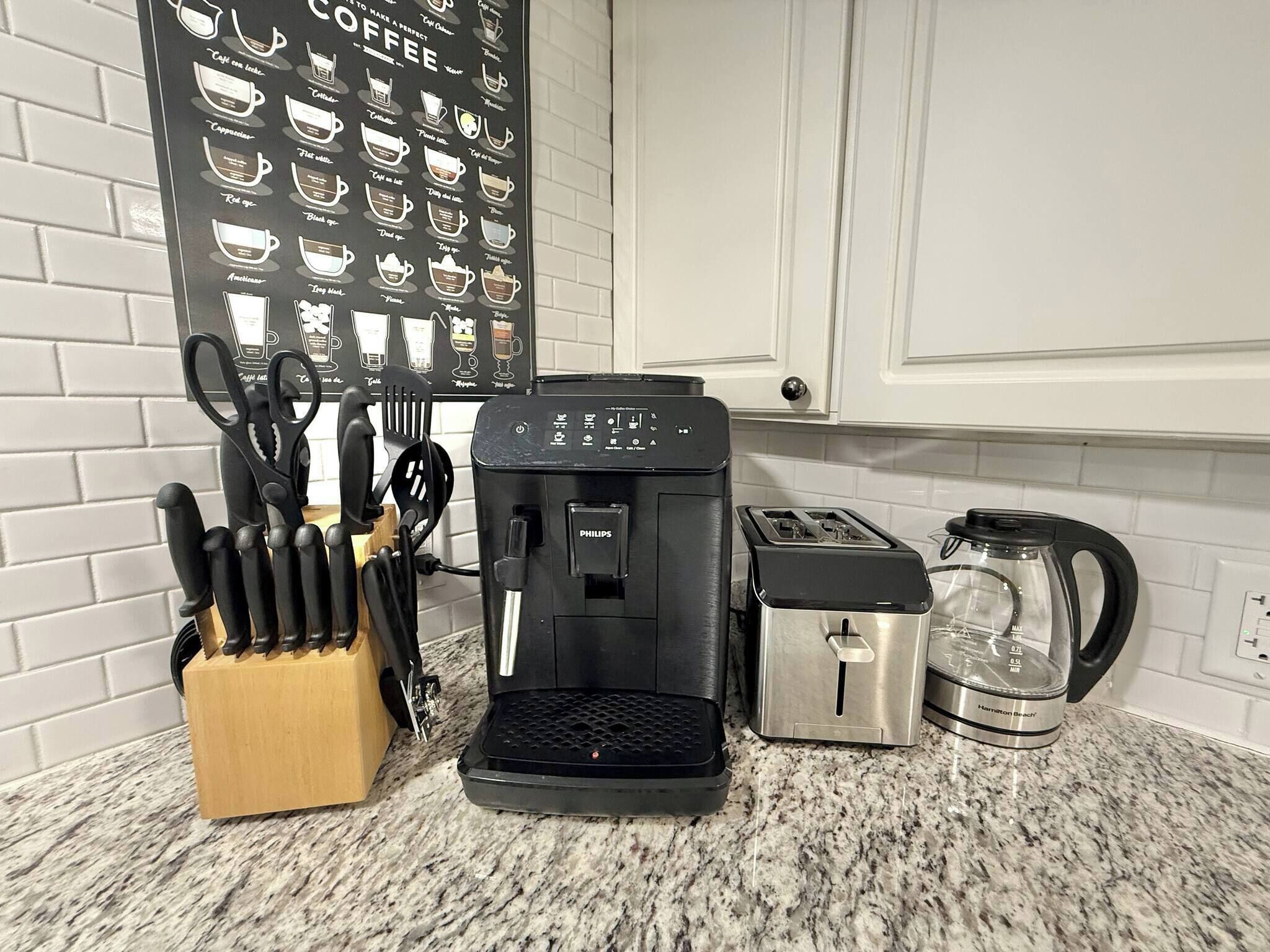 A kitchen with a coffee maker, toaster, and kettle, along with a knife block and a coffee-themed wall.