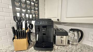A kitchen with a coffee maker, toaster, and kettle, along with a knife block and a coffee-themed wall.