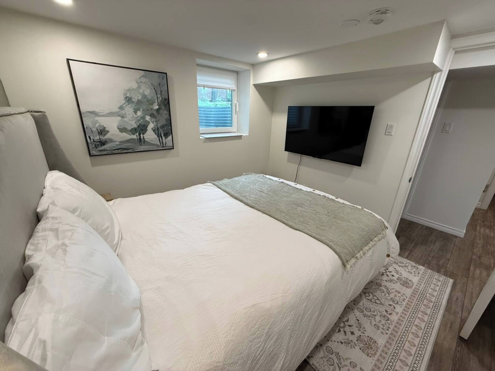 Ein Schlafzimmer mit einem Bett, einem an der Wand montierten Fernseher, einem Fenster und einer Tür.