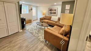 A living room with a sofa, coffee table, and a lamp. There is a door leading to another room and a window with blinds.