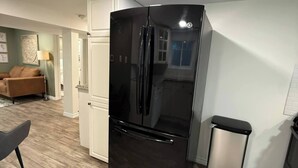 A modern kitchen with a black refrigerator, a trash bin, and a dining area with a chair.