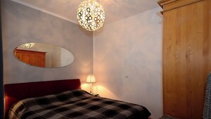 A bedroom with a bed, a mirror, a lamp, and a wardrobe. - Exclusive 2-room apartment in a prime location on Neumarkt (Dresden)