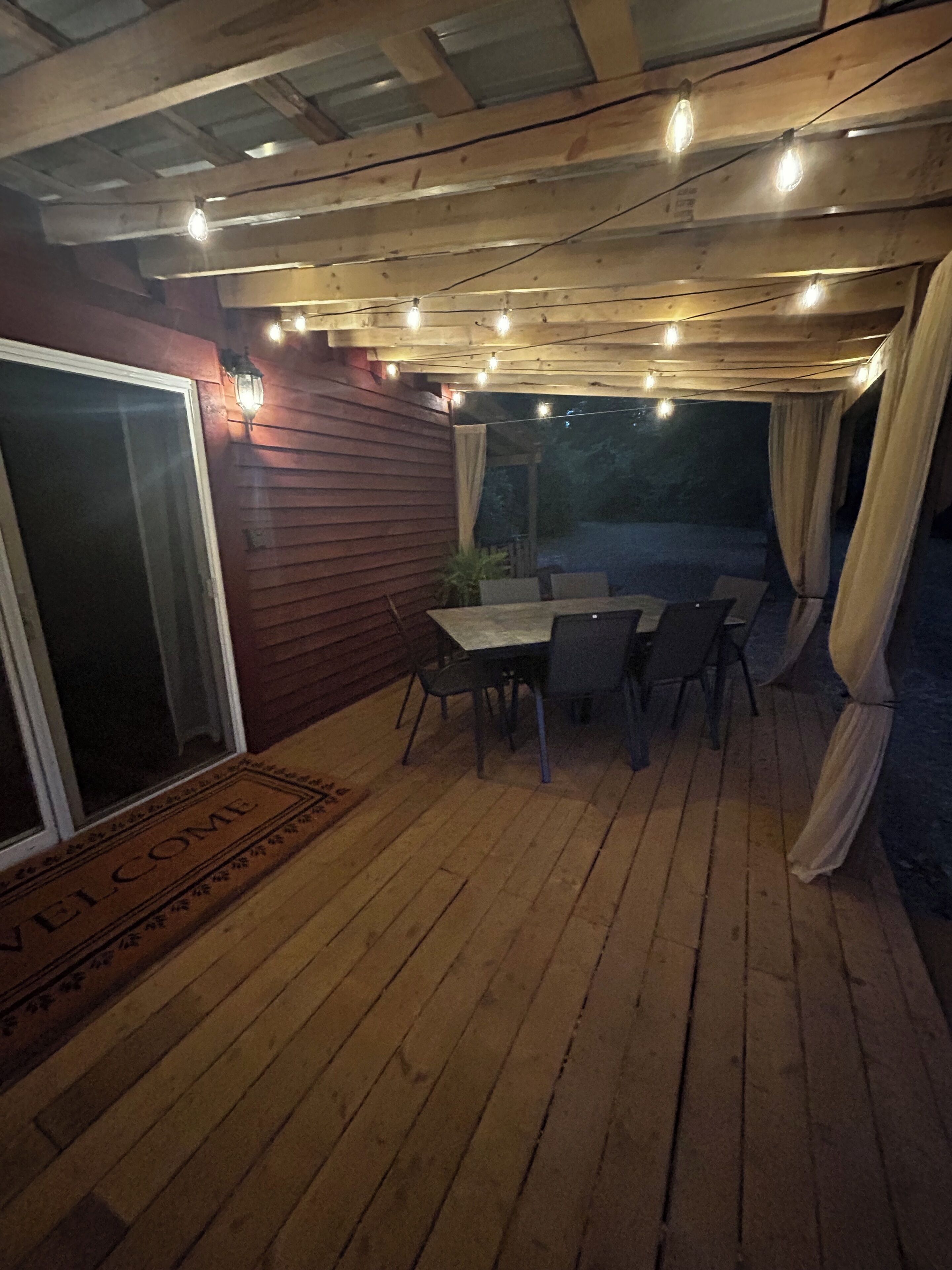 A wooden deck with a table and chairs, a sliding glass door, and string lights.
