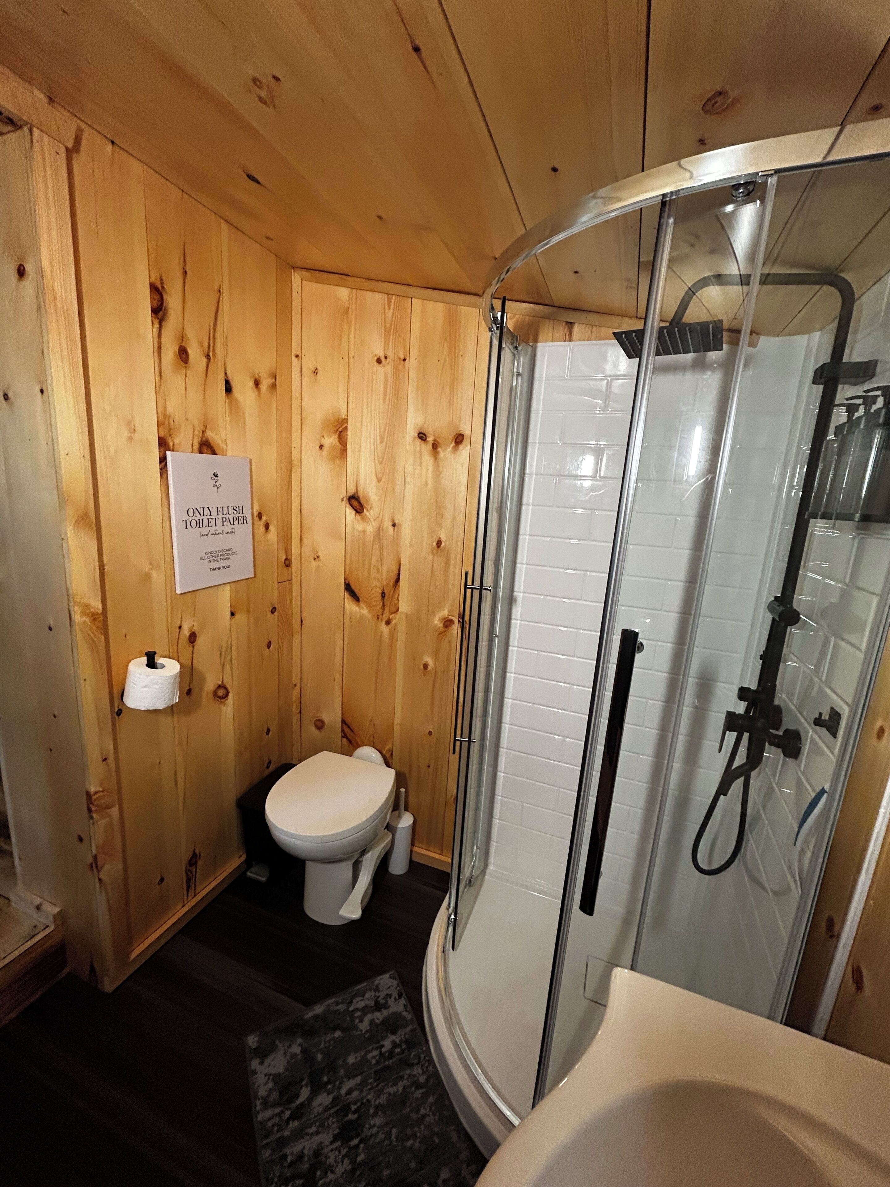 Een houten badkamer met toilet, een douchecabine van glas, en een bordje met de tekst 'uitsluitend toiletpapier gebruiken'.