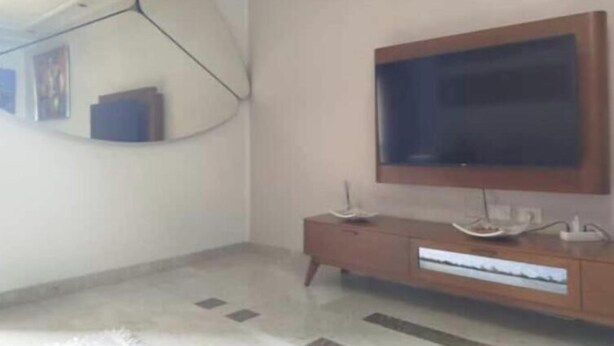 Ein Zimmer mit einem an einer Holzkommode befestigten Fernseher, einem Spiegel an der Wand und einem gemusterten Teppich auf dem Boden.