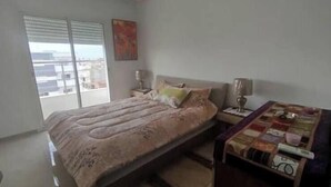 Ein Schlafzimmer mit einem Bett, einem Nachttisch, einer Lampe und einem Fenster mit Jalousien.