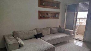 Ein Wohnzimmer mit Ecksofa, einem kleinen Tisch und einer Schiebetür zu einem Balkon.