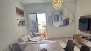 Ein Essbereich mit einem langen Tisch, Stühlen, einer Kristallleuchtre und einem Fernseher.