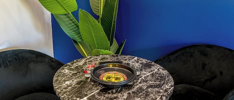 A round table with a marble top, surrounded by black chairs, against a blue wall with large green plants.