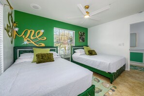 Une chambre avec deux lits, des murs verts, un ventilateur de plafond et une fenêtre.