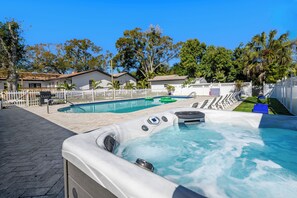 Um quintal com hidromassagem, piscina e um espaço de pátio cercado.