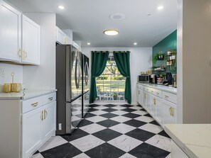 A kitchen with white cabinets, a black and white checkered floor, a refrigerator, and a window with green curtains. - 12 BR Estate!•HeatedPool • Pickle • GameRm •Events (Clearwater)