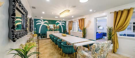 Uma área de refeições com uma mesa comprida, cadeiras cor turquesa e um banco estampado.