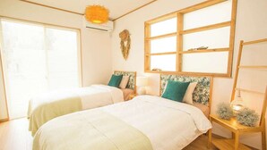 A room with two beds, a window, a hanging light fixture, and a wooden shelf with decorative items. - Resort House Daisho G Uruma (Uruma)