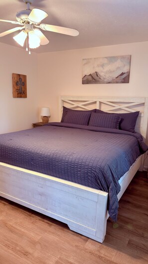 Un dormitorio con cama, ventilador de techo, un cuadro y una lámpara de noche.