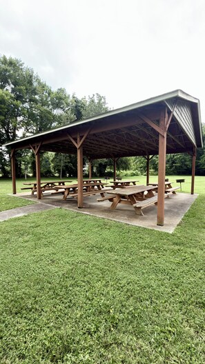 A covered picnic area with multiple wooden picnic tables and a concrete floor. - River Pointe Getaway - Pigeon Forge Home + River Access, 3 Mins to the Parkway (Pigeon Forge)
