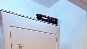 Una lavadora de carga frontal con panel de control, un secador encima y un pequeño estante con objetos.