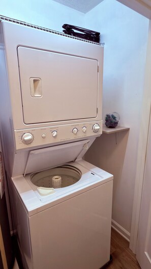 Eine Waschmaschine mit Frontlader, ein Trockner darauf und eine kleine Ablagefläche mit Gegenständen.