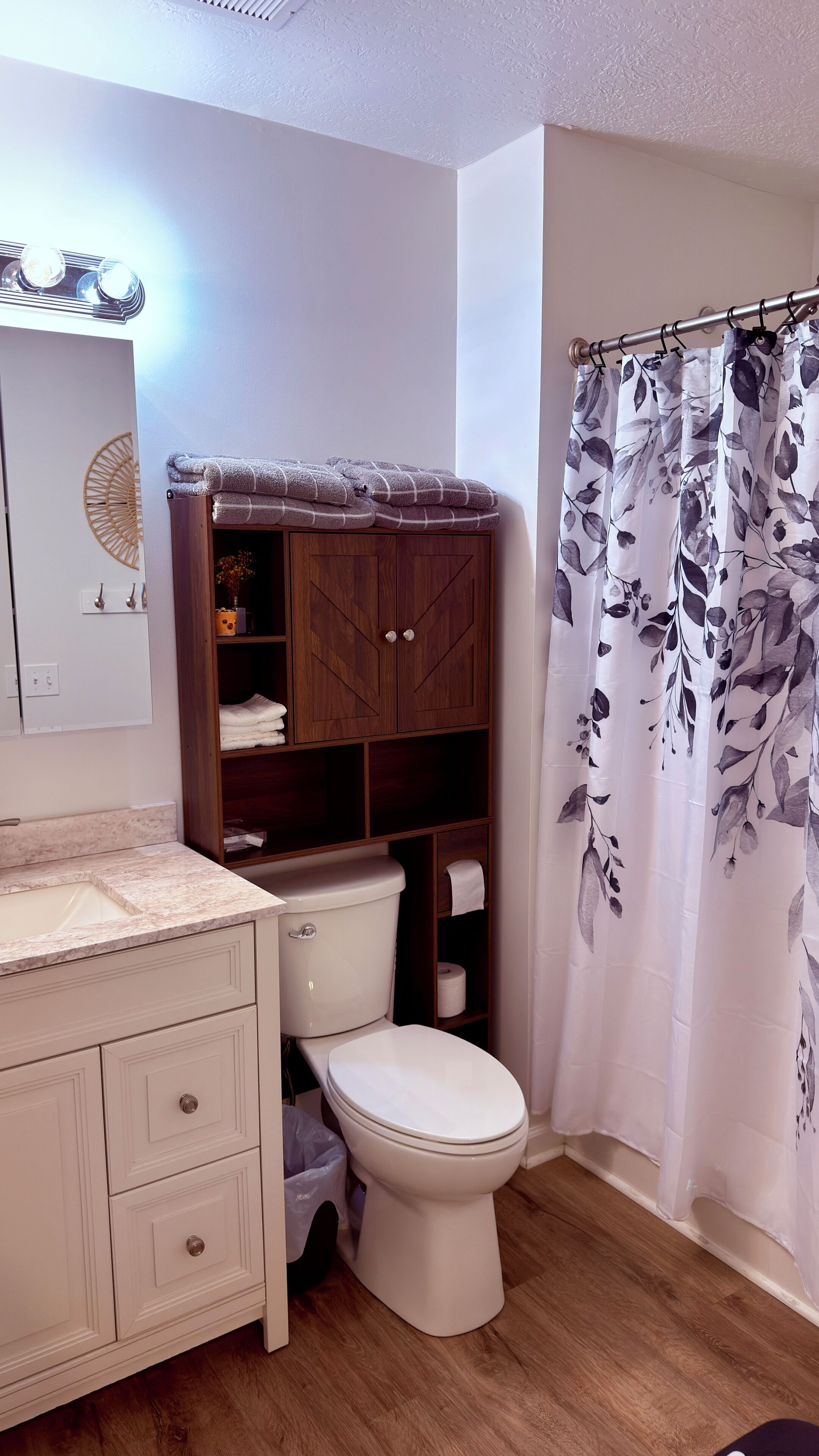 A bathroom with a toilet, a wooden cabinet, a marble countertop, and a shower curtain with a floral pattern.