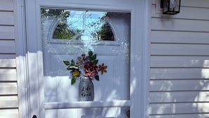 Puerta blanca con un panel de vidrio, felpudo y una pequeña ventana con una lámpara encima.