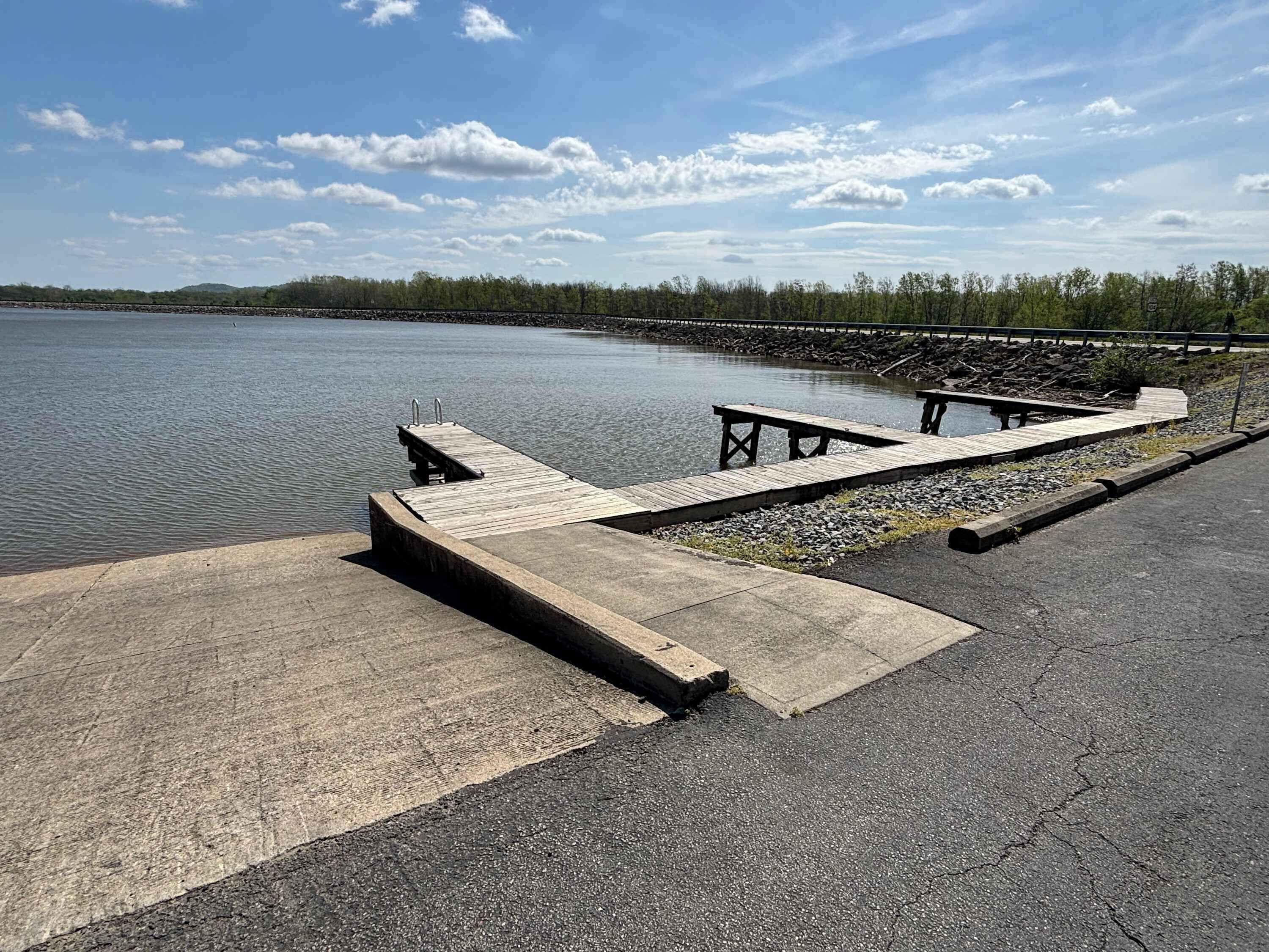 Un muelle de hormigón que se adentra en aguas tranquilas, con un camino pavimentado a su lado.