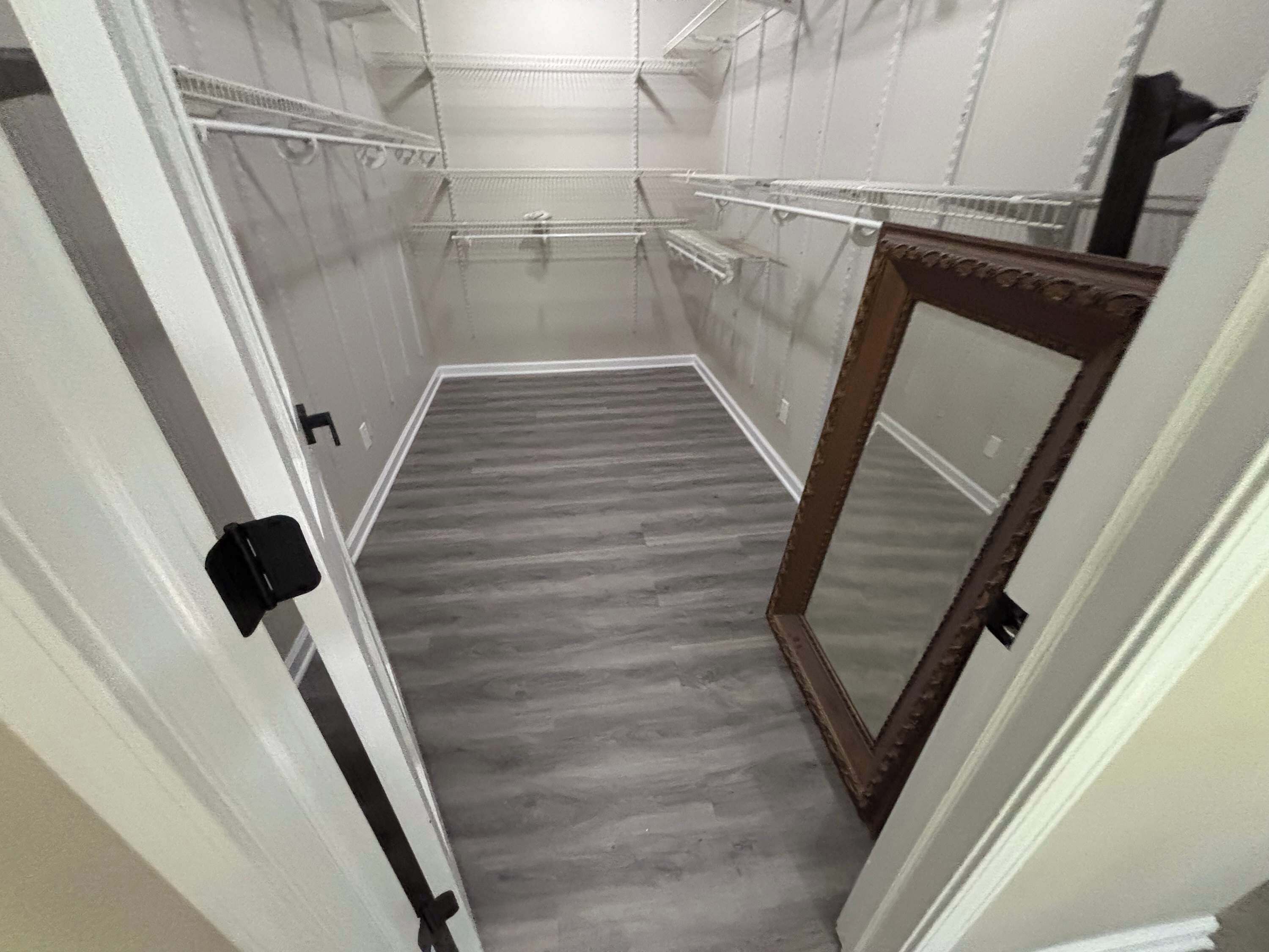 A narrow walk-in closet with wooden flooring, metal shelving, and a mirror.