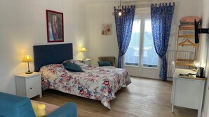 Ein Schlafzimmer mit einem Bett, Nachttischen, einer Kommode, einem Sessel und einem Fenster mit Vorhängen.