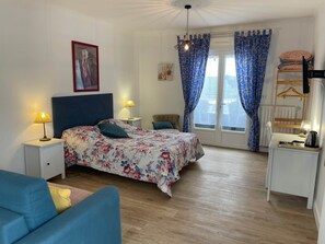 Ein Schlafzimmer mit einem Bett, Nachttischen, einer Kommode, einem Sessel und einem Fenster mit Vorhängen.
