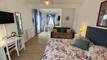 Un dormitorio con cama, escritorio, silla, televisión y una kitchenette al fondo.