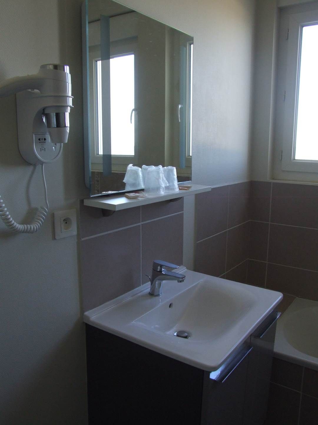 Un baño con lavamanos, espejo y secador de pelo montado en la pared.