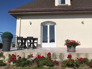 A building with a white exterior, a door with glass panels, a balcony with chairs, and potted plants. - Beachfront studio with a terrace, perfect for couples, families, or groups of friends (Saint-Côme-de-Fresné)