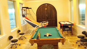 Een biljartzaal met een pooltafel, een tafelvoetbaltafel en een hangmat.