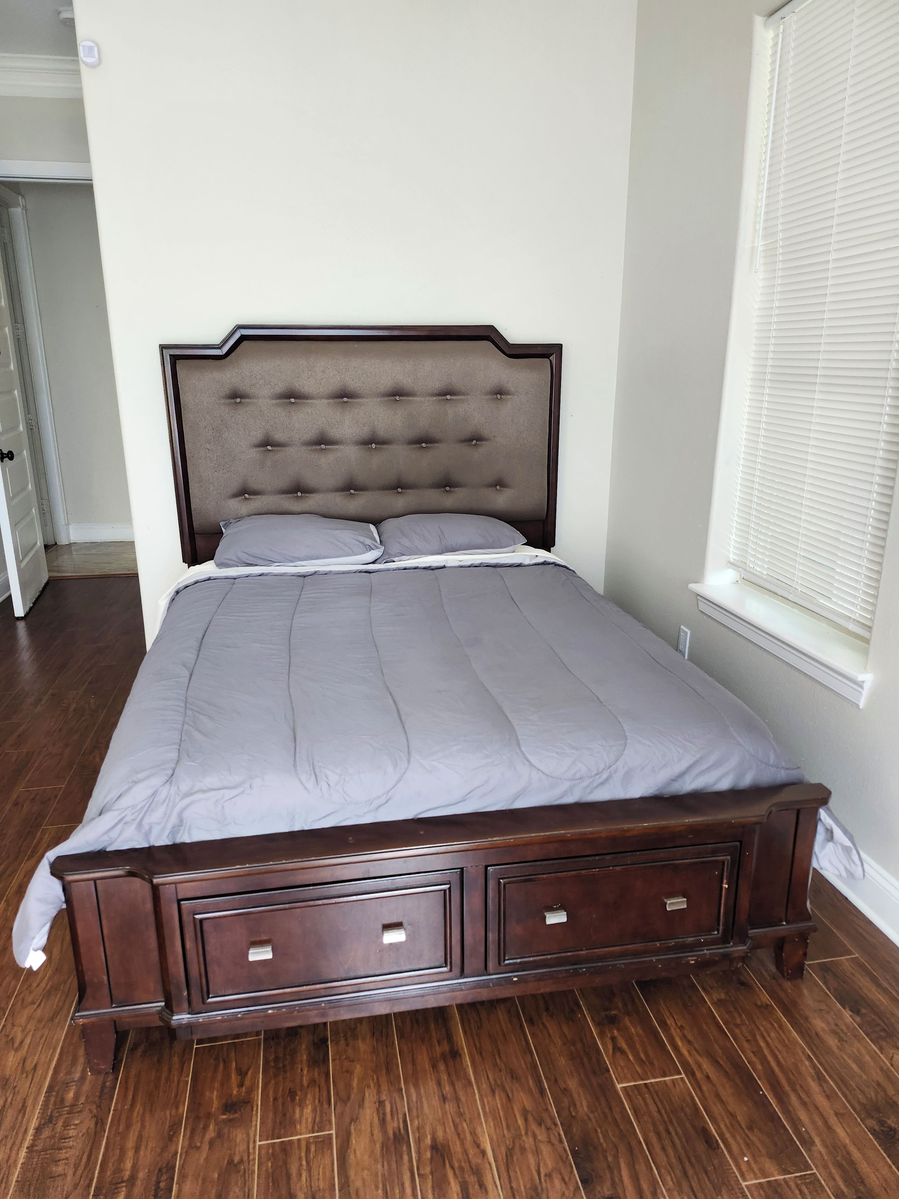 A bedroom with a large bed, wooden headboard, and a window with blinds.
