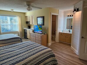 Ein Schlafzimmer mit zwei Betten, einem Deckenventilator, einem Fernseher und einer Küchenzeile.