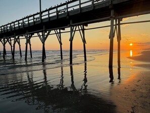 A pier extending over a beach with the sun setting in the background. - The Retreat at Sunset Beach/Elegant Coastal Condo with Pools & Hot Tub (Sunset Beach)