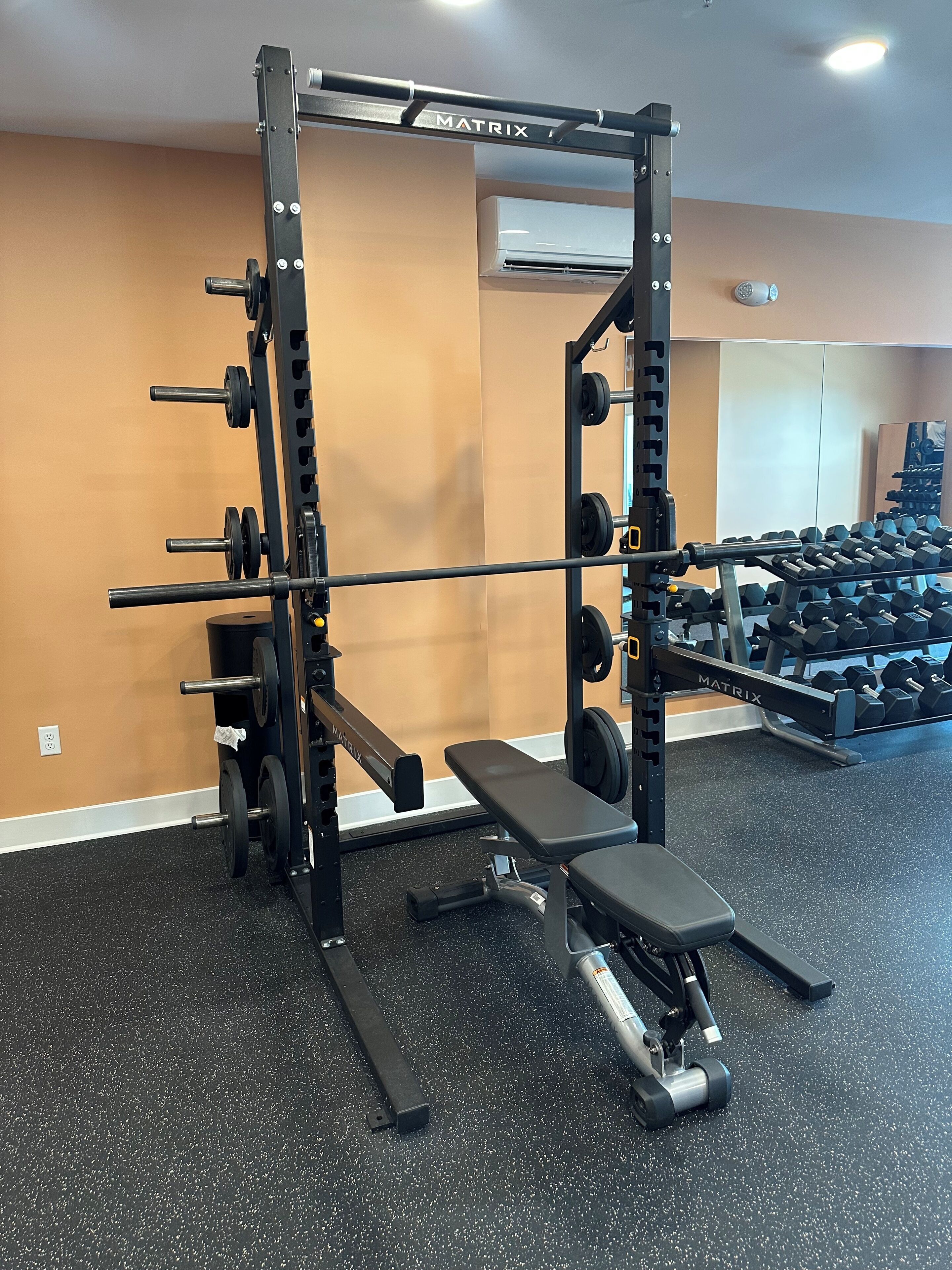 A gym with weightlifting equipment, a bench, and a wall-mounted air conditioner.