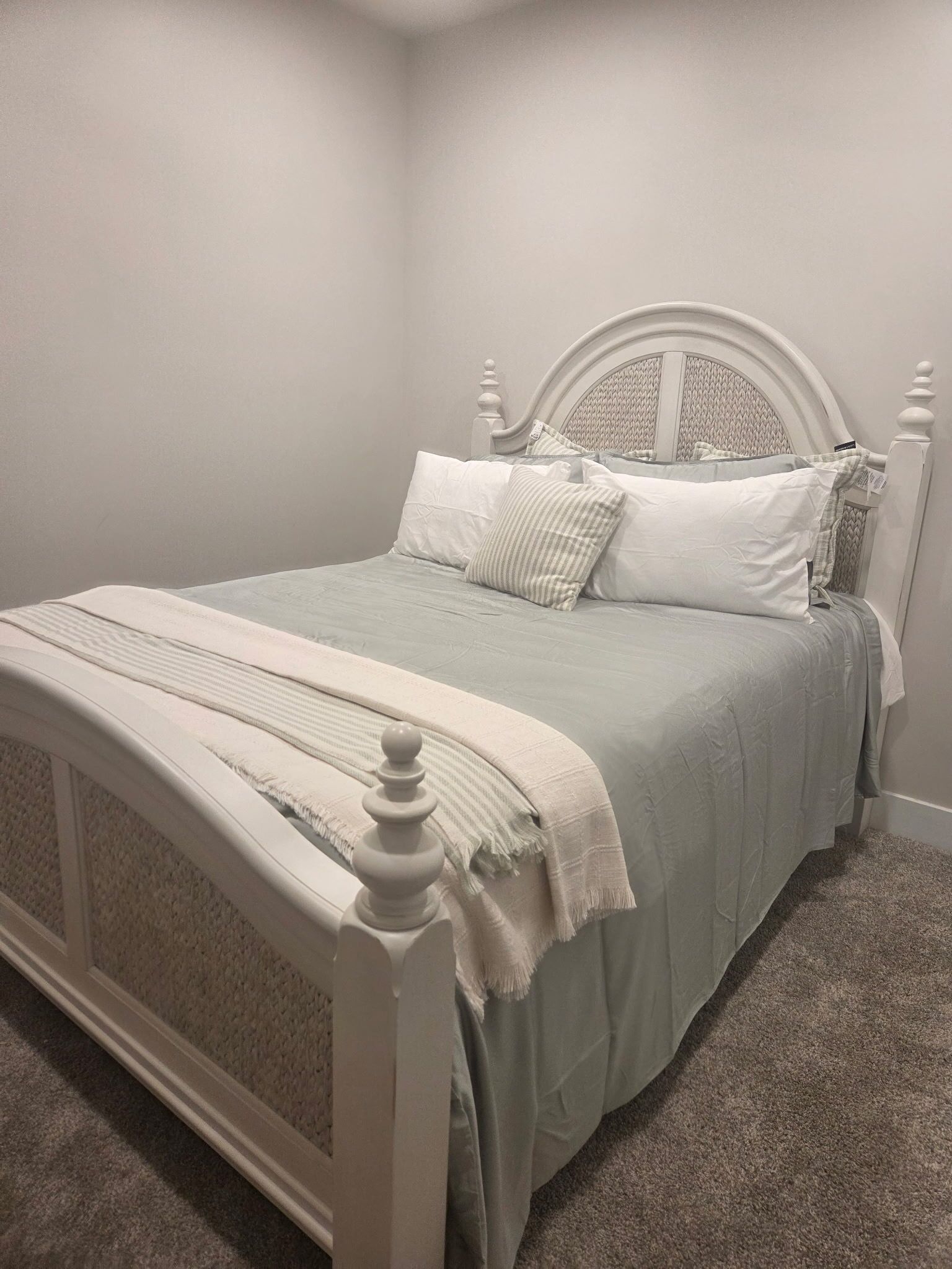 A single-bed room with a white headboard, a grey bedspread, and a white throw blanket.