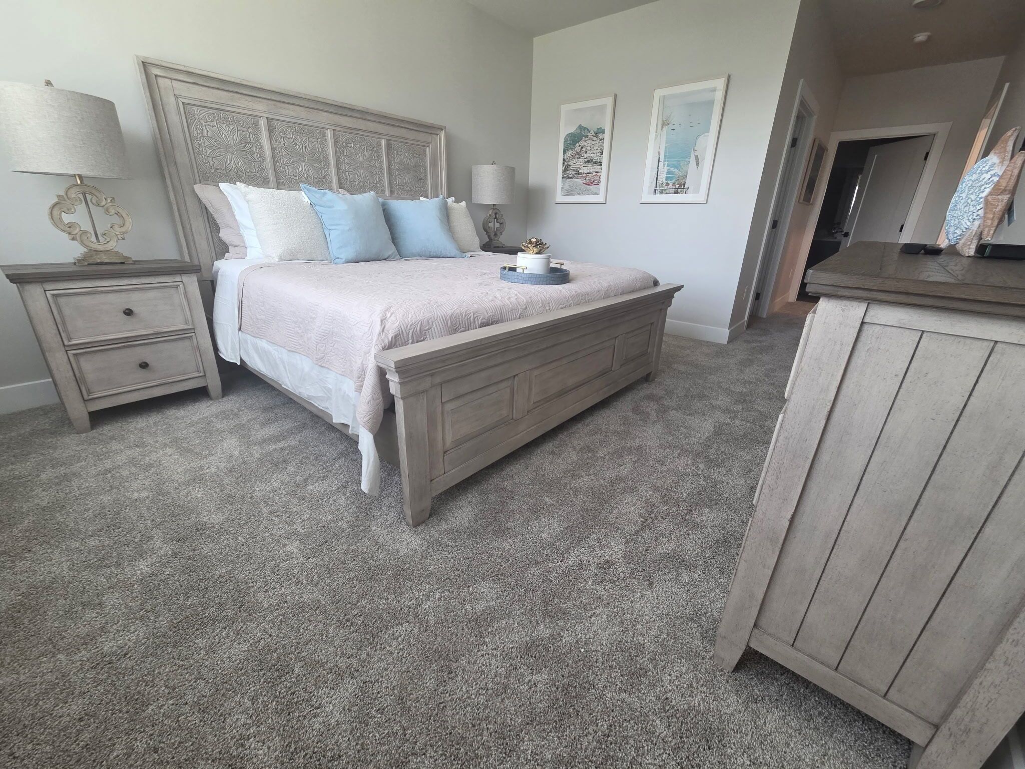 A bedroom with a bed, nightstands, a dresser, and wall art.