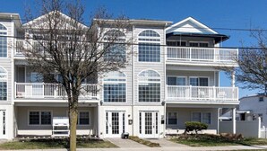 A multi-story residential building with balconies, large windows, and a tree in the foreground. - New 3BR Wildwood Condo • Sleeps 8 • Garage • Walk to Beach (Wildwood)