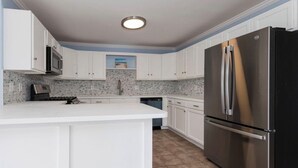 A kitchen with white cabinets, a stainless steel refrigerator, a microwave, and a tiled backsplash. - New 3BR Wildwood Condo • Sleeps 8 • Garage • Walk to Beach (Wildwood)