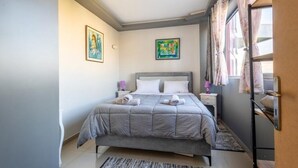 A bedroom with a bed, a nightstand, a lamp, and artwork on the walls. - A space of comfort and relaxation with a wonderful view and warm hospitality. (Markopoulo Mesogeas)